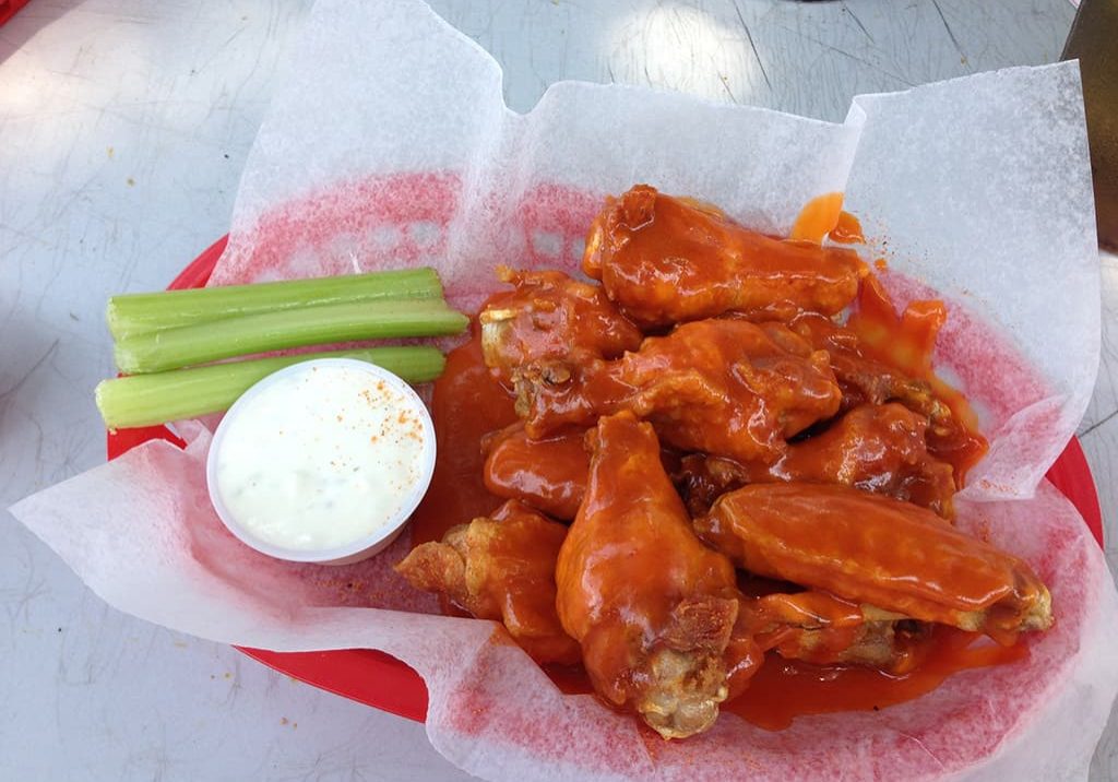 A basket of buffalo wings served with celery sticks and a cup of ranch dressing on a table.