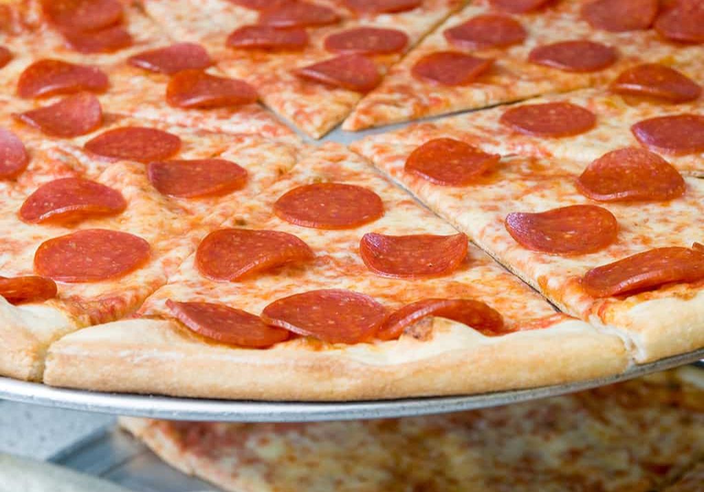 A large pepperoni pizza with slices evenly cut, displayed on a metal tray.